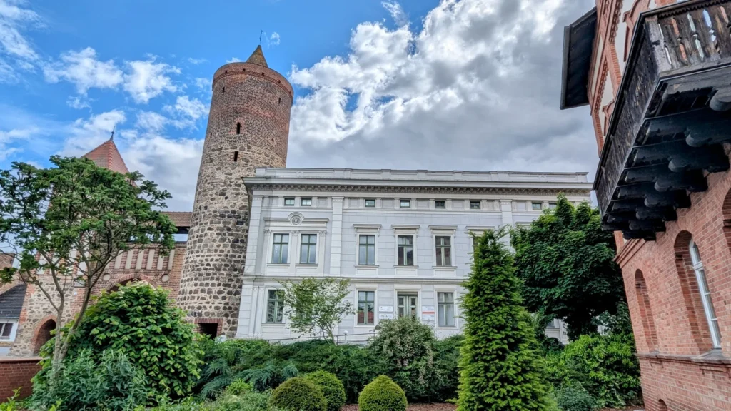 Zinnaer Tor in Jüterbog, ein gemauerter Rundturm hinter einem hellen Altbau