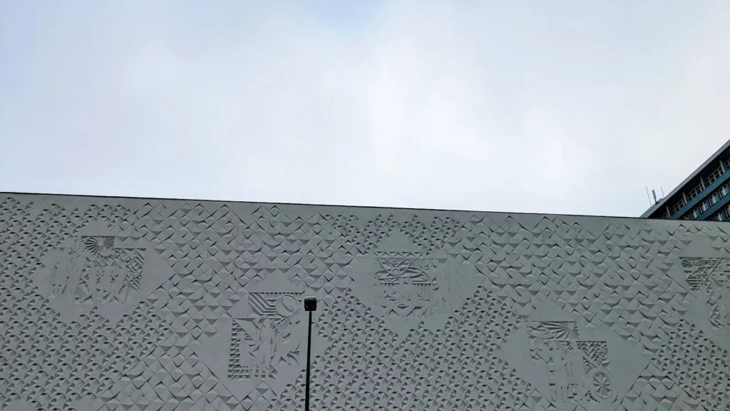Betonrelief mit Rautenmuster und Figuren an einer Außenwand des Kinos International