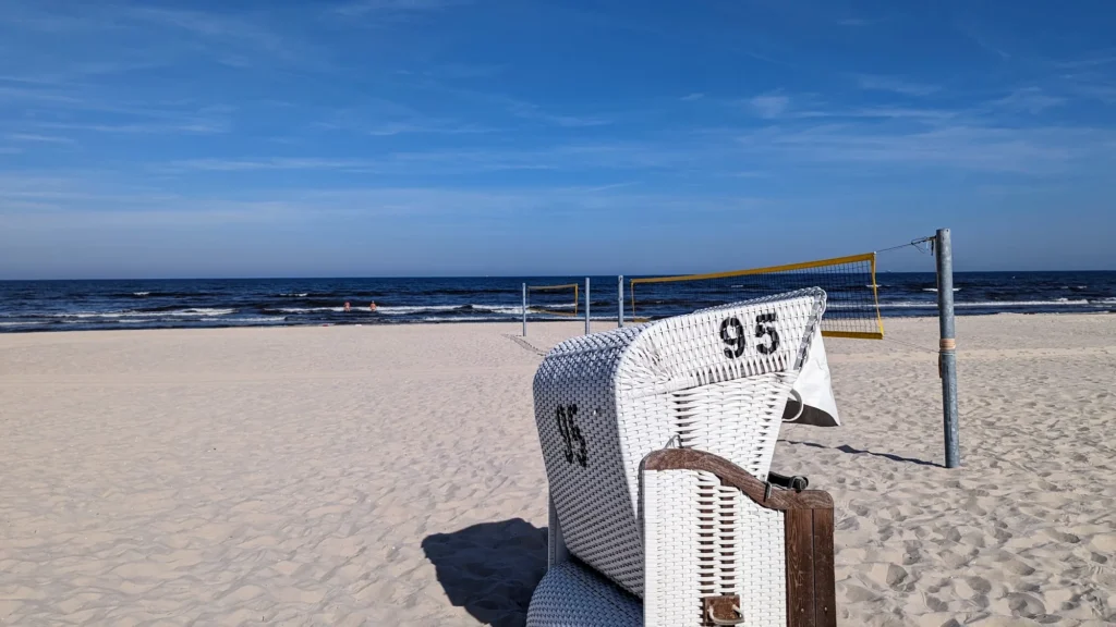 Weißer Strandkorb mit der Nummer 95 am Strand, dahinter ein Volleyballnetz und die Ostsee
