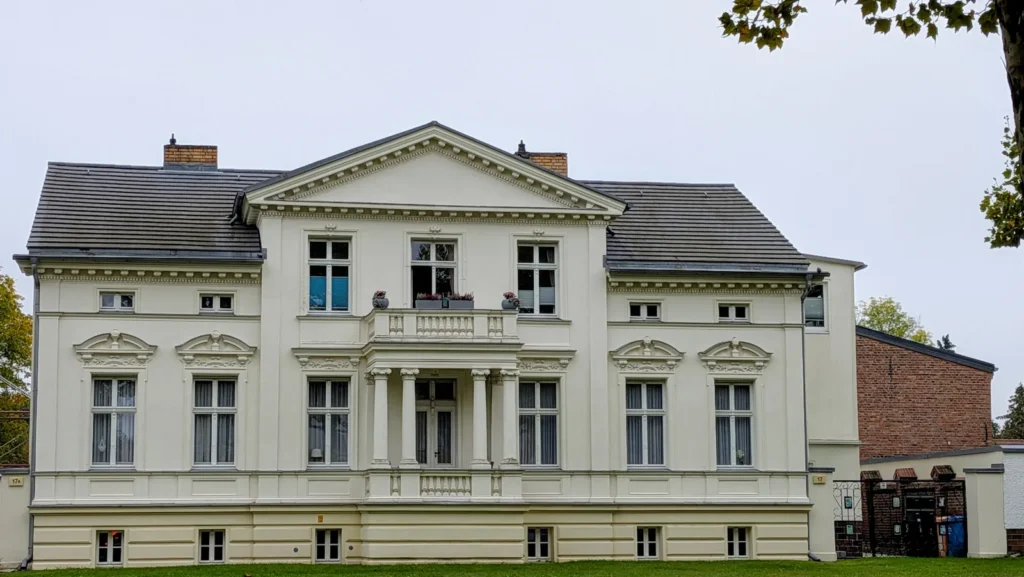Weißes Haus mit Giebel und Balkon an der Straße Alt-Karow