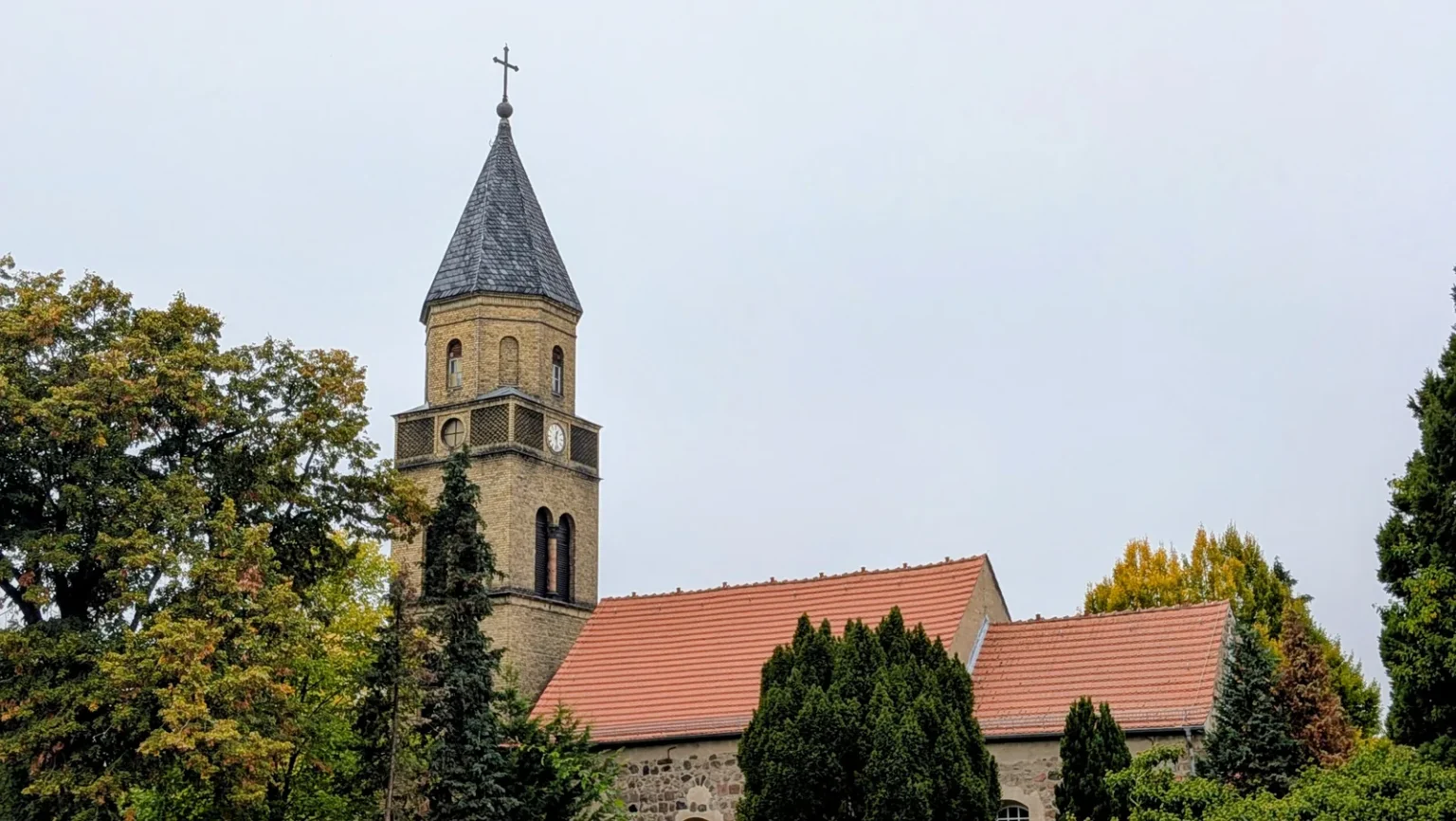 Dorfkirche Karow mit Backsteinturm und rotem Dach zwischen Bäumen