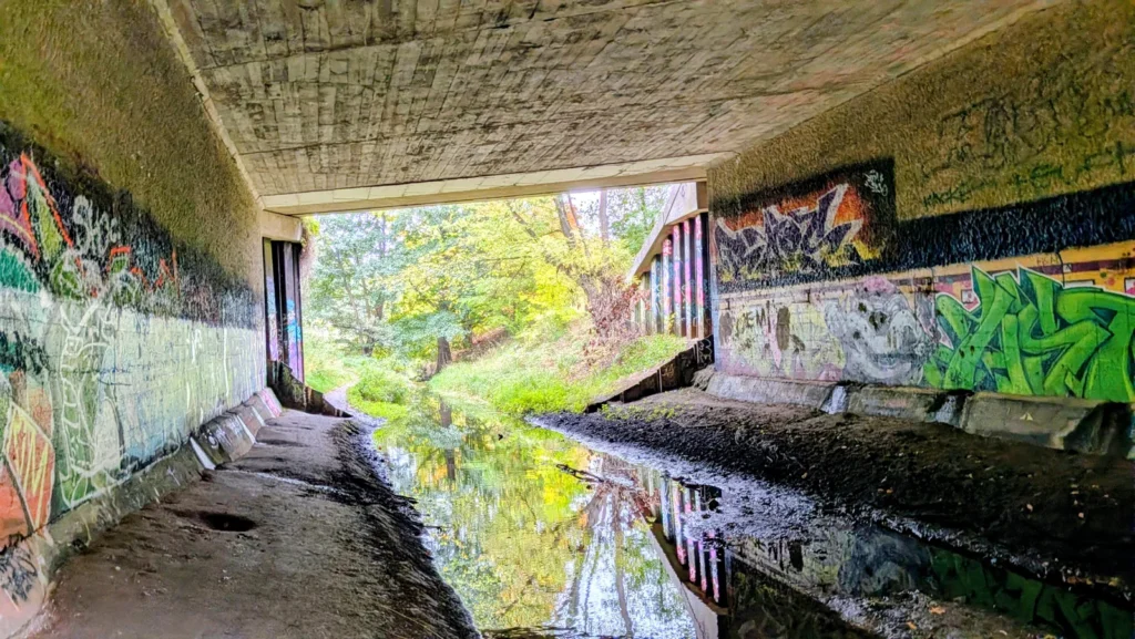 Betondurchlass mit Graffiti, durch den ein Graben fließt, bei Karow