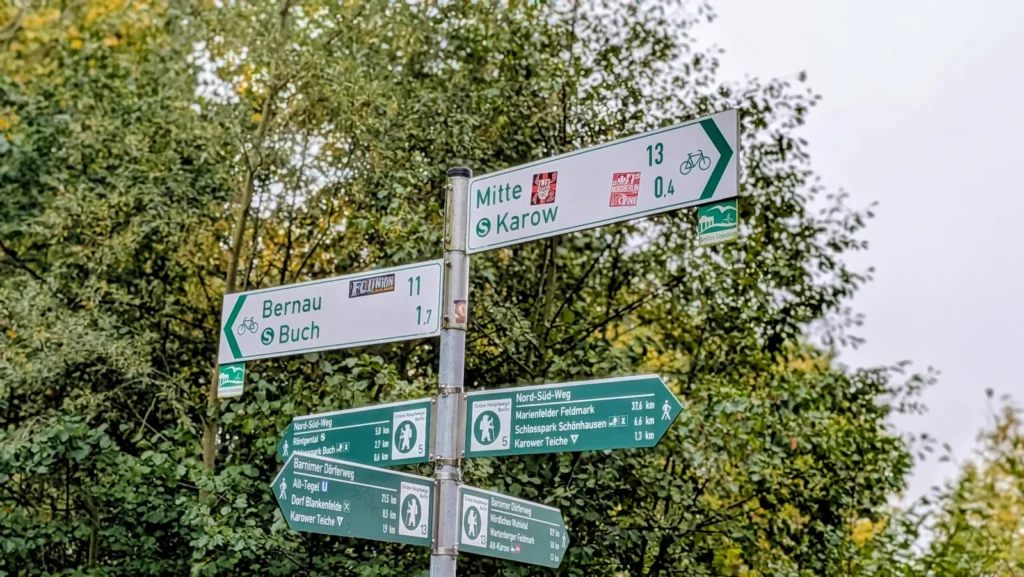 Grün-weißer Wegweiser mit Nord-Süd-Weg, Barnimer Dörferweg und Karower Teichen