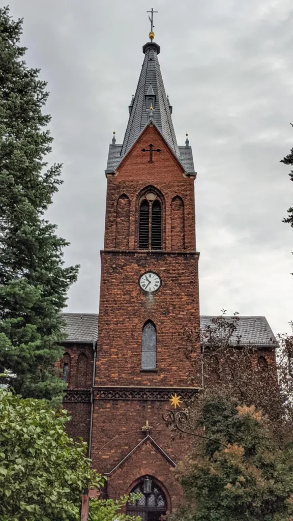 Backsteinturm der Jesuskirche in Kaulsdorf mit Turmuhr, spitzem Helm und Spitzbogenportal