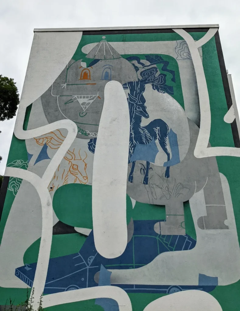 Wandbild Aoi von Klub7 an der Stadthalle in Lutherstadt Wittenberg: abstrakte grüne, graue und blaue Flächen mit weißen Linien an einem Wohnblock