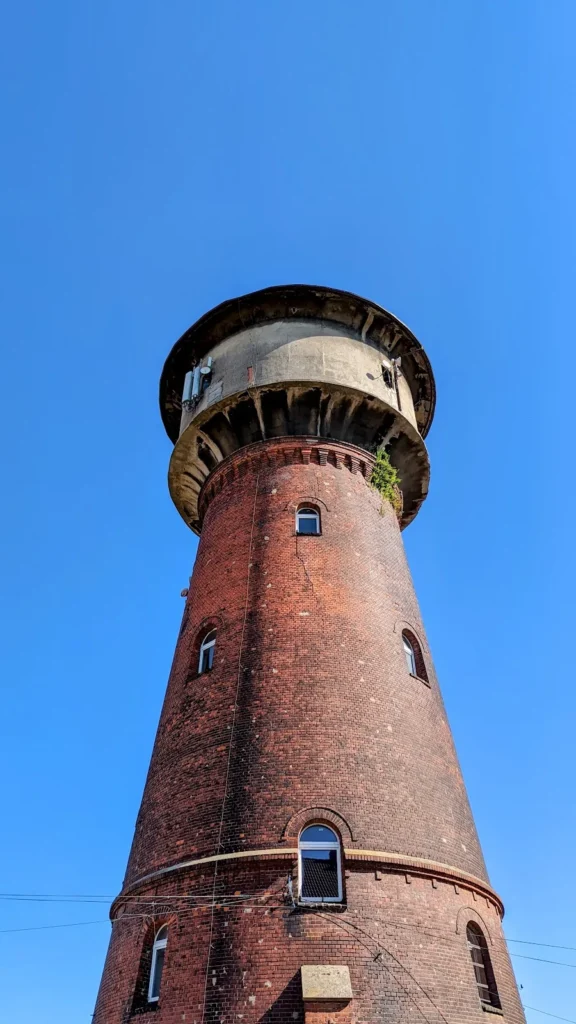 Runder Wasserturm aus rotem Backstein mit hell verputztem, auskragendem Behälter in Kostrzyn nad Odrą vor wolkenlosem Himmel