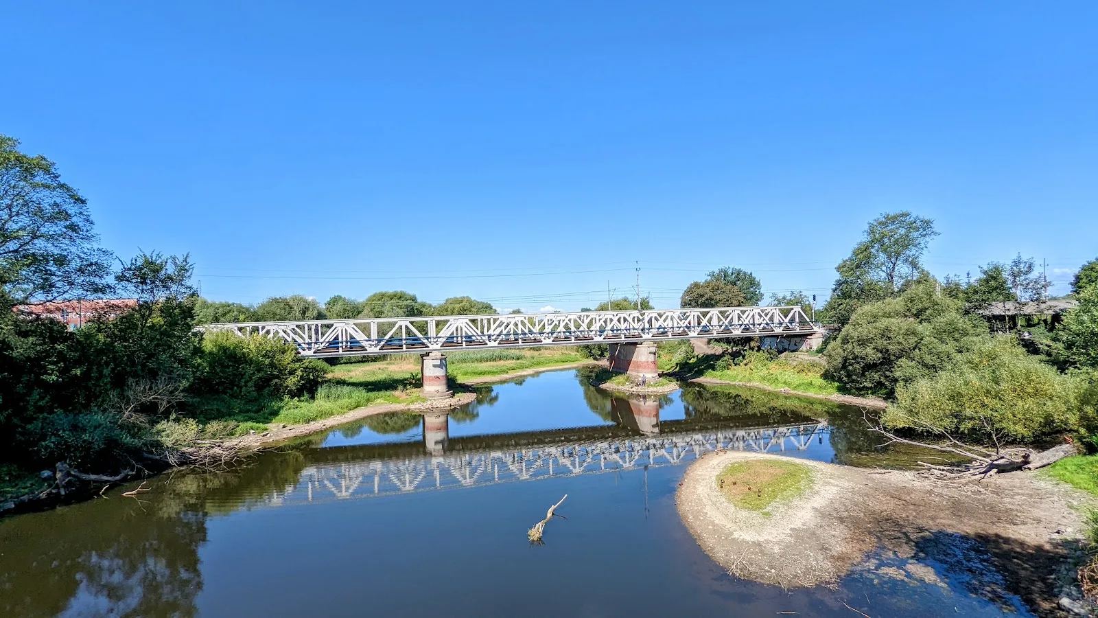Altarm der Warthe in Kostrzyn nad Odrą mit Sandbank bei Niedrigwasser, dahinter eine weiße Stahlbrücke auf gemauerten Pfeilern