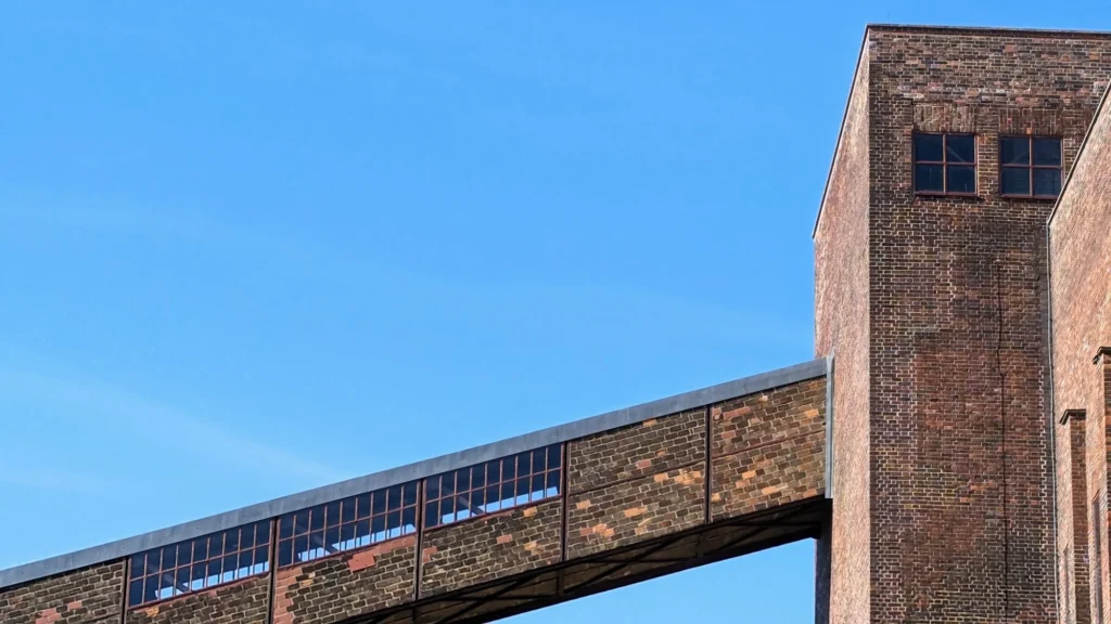 Geschlossene Bandbrücke führt schräg in einen Backsteinturm des Kraftwerks