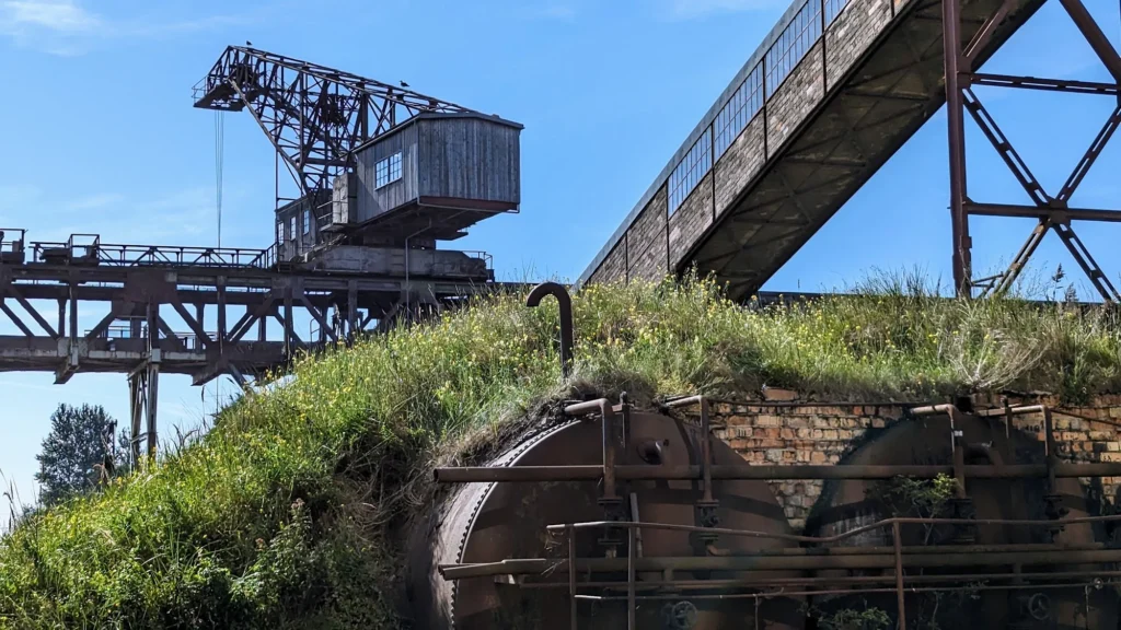 Kranbrücke und schräges Förderband über einem grasbewachsenen Ziegelbau