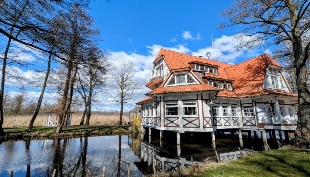 Weißes Holzhaus mit rotem Dach auf Pfählen im Wasser, die Seelodge am Kremmener See