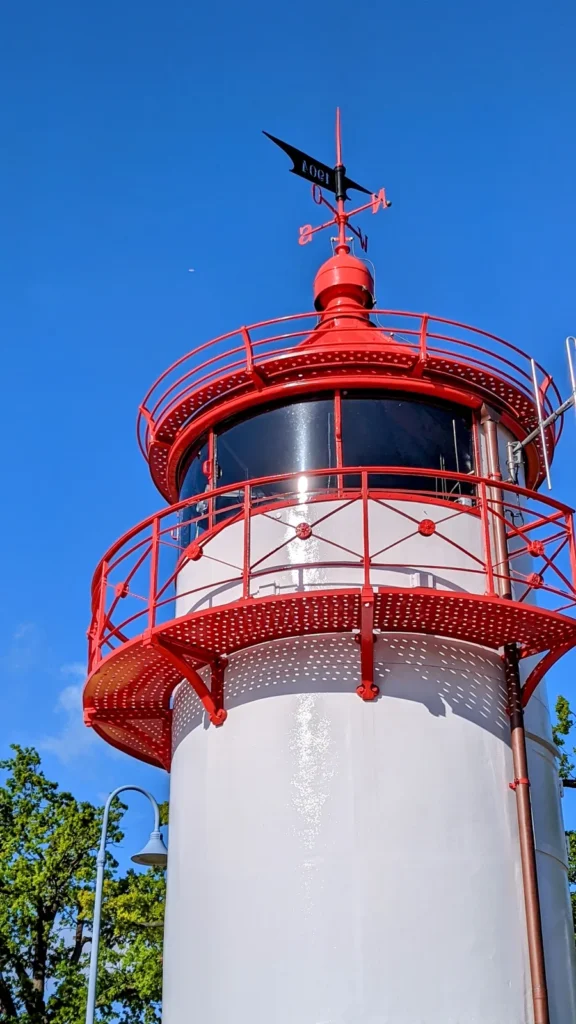 Kleiner weißer Leuchtturm mit roter Galerie und Wetterfahne am Hafen Lauterbach