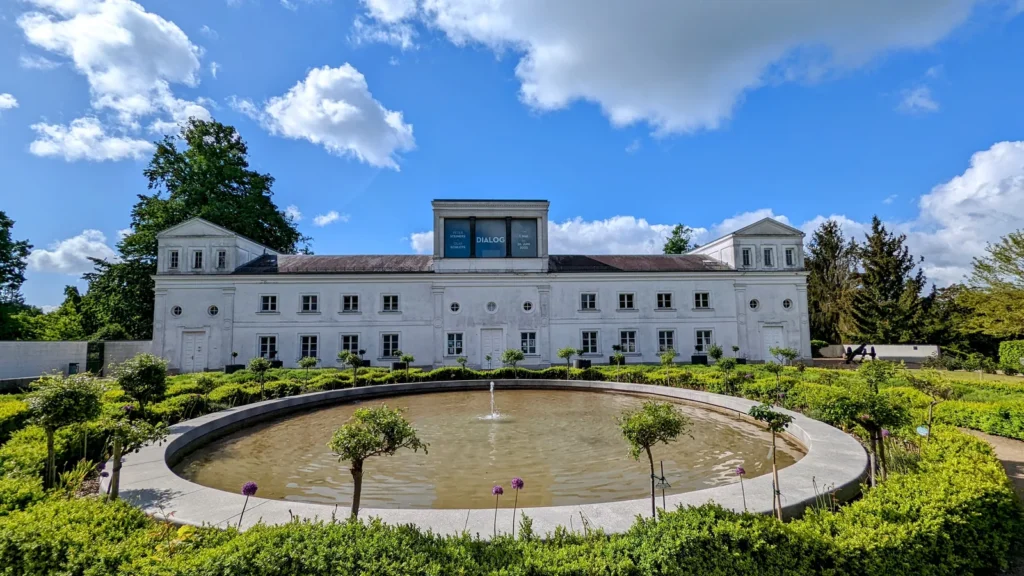 Weiße Orangerie Putbus mit rundem Wasserbecken und Beeten davor