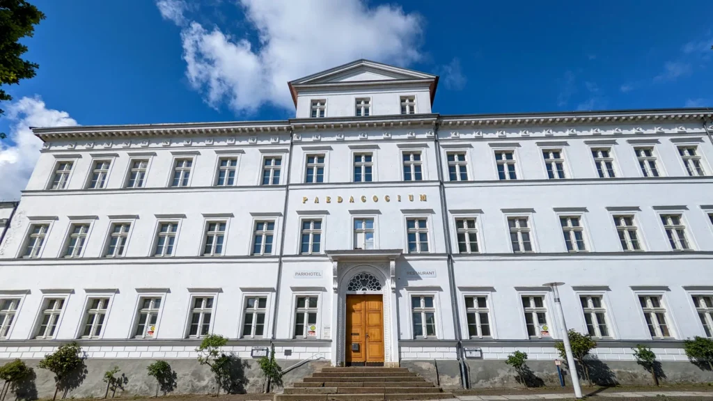 Langgestrecktes weißes Gebäude des Pädagogiums Putbus mit Portal und Freitreppe