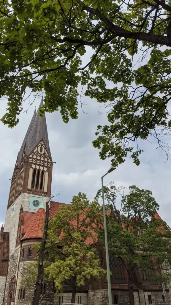 Backsteinkirche mit spitzem Turm hinter Bäumen am Roedeliusplatz, heute koptisch-orthodoxe Kirche