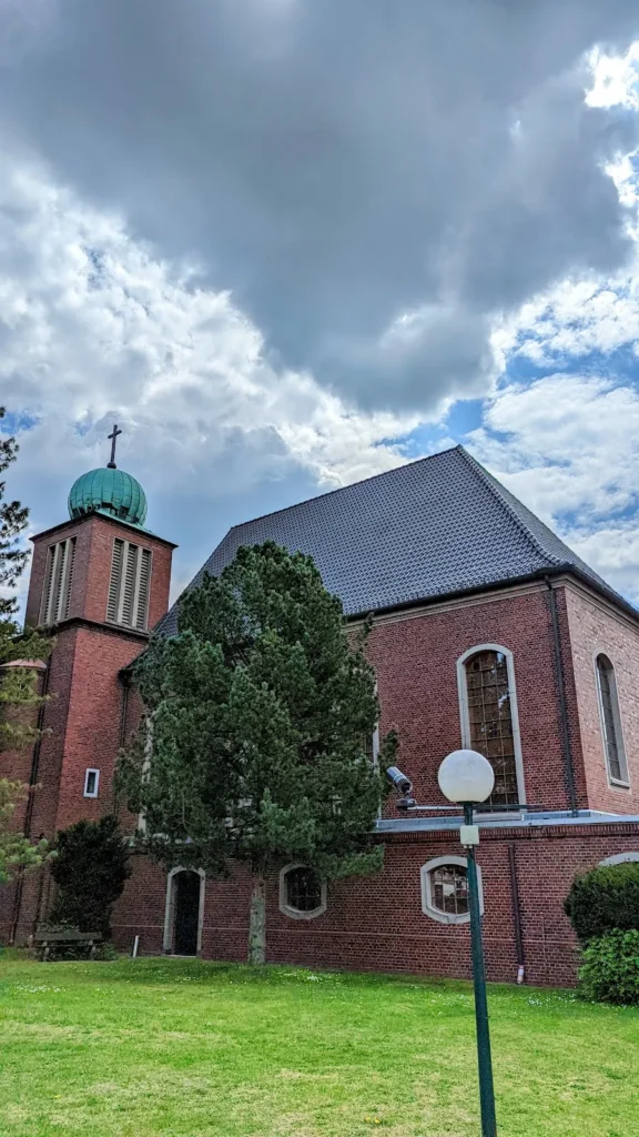 Backsteinkirche mit Kupferkuppel auf dem Turm und dunklem Dach, Rasenfläche davor, Lichtenrade