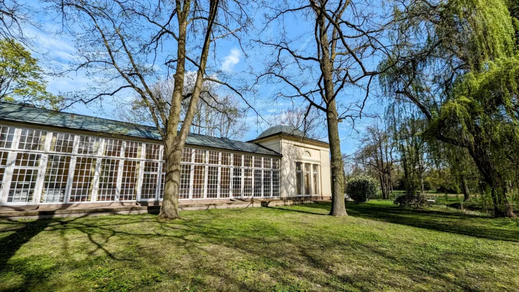Orangerie im Schlosspark Lübbenau, langgestrecktes Gebäude mit großen Fenstern hinter einer Wiese