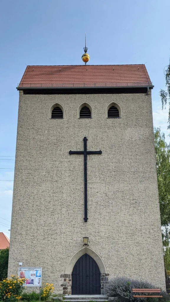 Backsteinkirche mit quadratischem Turm, großem dunklem Kreuz und Spitzbogenportal, die Kreuzkirche in Mahlsdorf