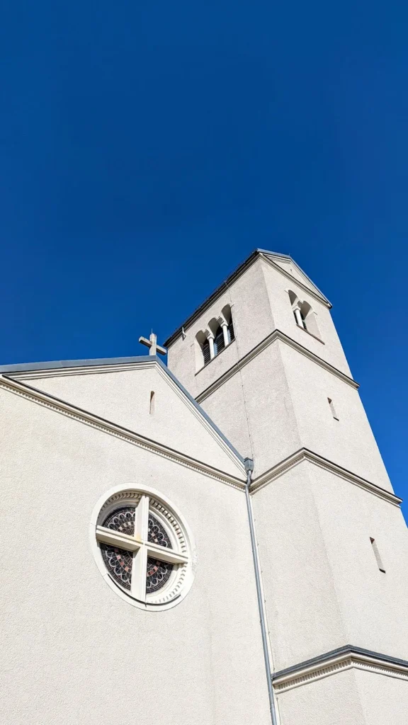 Weiße Kirche St. Alfons mit Turm und rundem Fenster unter blauem Himmel in Marienfelde