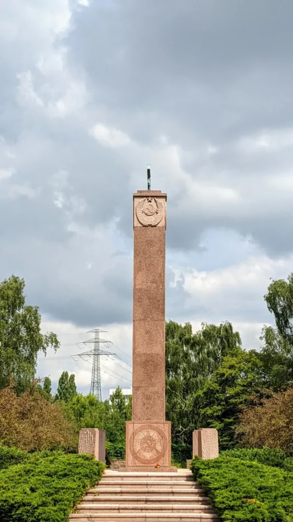 Obelisk aus rötlichem Stein mit Treppe und Heckenbeeten im Sowjetischen Ehrenhain auf dem Parkfriedhof Marzahn