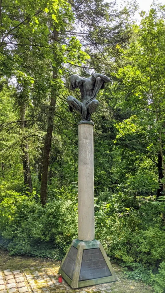 Bronzefigur auf hoher Stele im Wald des Parkfriedhofs Marzahn, Denkmal für Zwangsarbeiter*innen