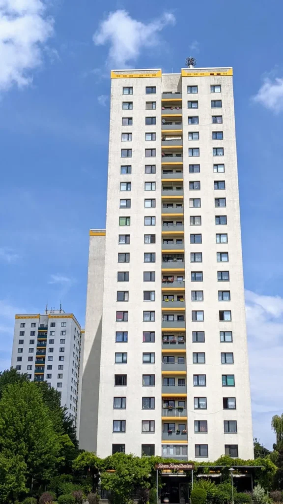 Etwa 16-geschossiges Plattenbau-Hochhaus hinter Bäumen in der Großsiedlung Marzahn