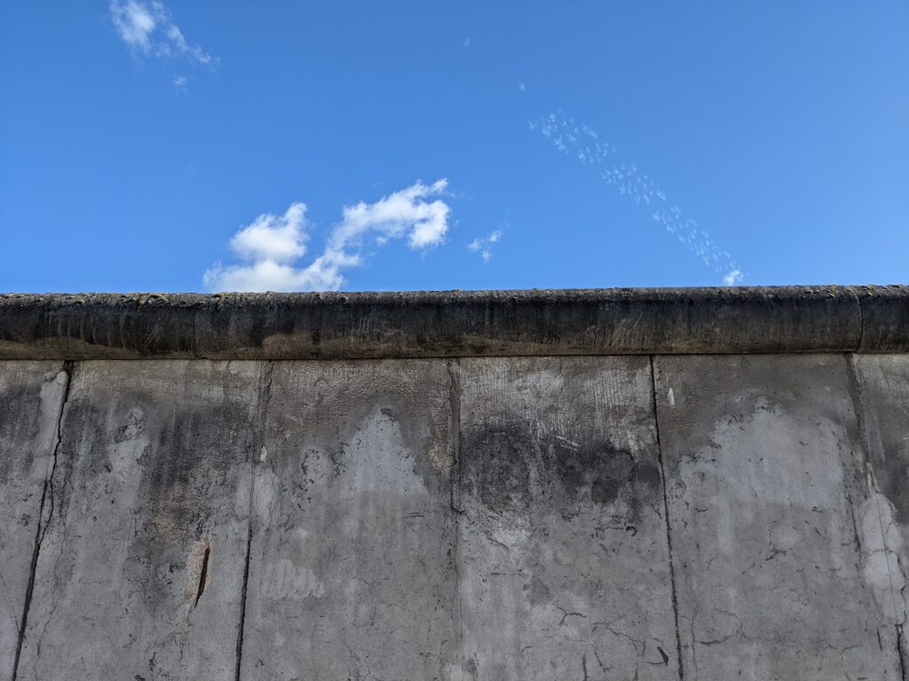Graue Betonsegmente der Berliner Mauer mit runder Mauerkrone vor blauem Himmel