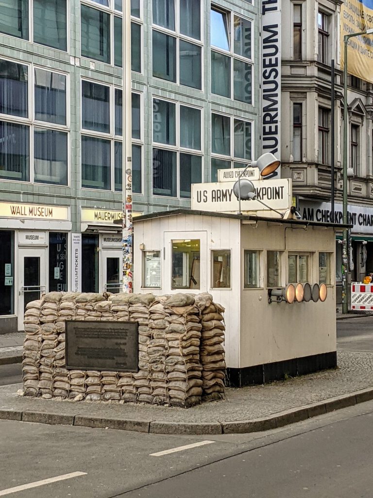 Weiße Kontrollbaracke mit der Aufschrift „US Army Checkpoint“ hinter einem Wall aus Sandsäcken