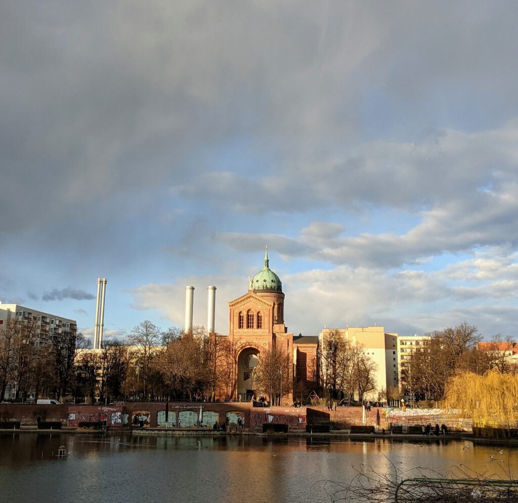 Wasserbecken im Abendlicht, dahinter die Backsteinkirche St. Michael mit grüner Kuppel