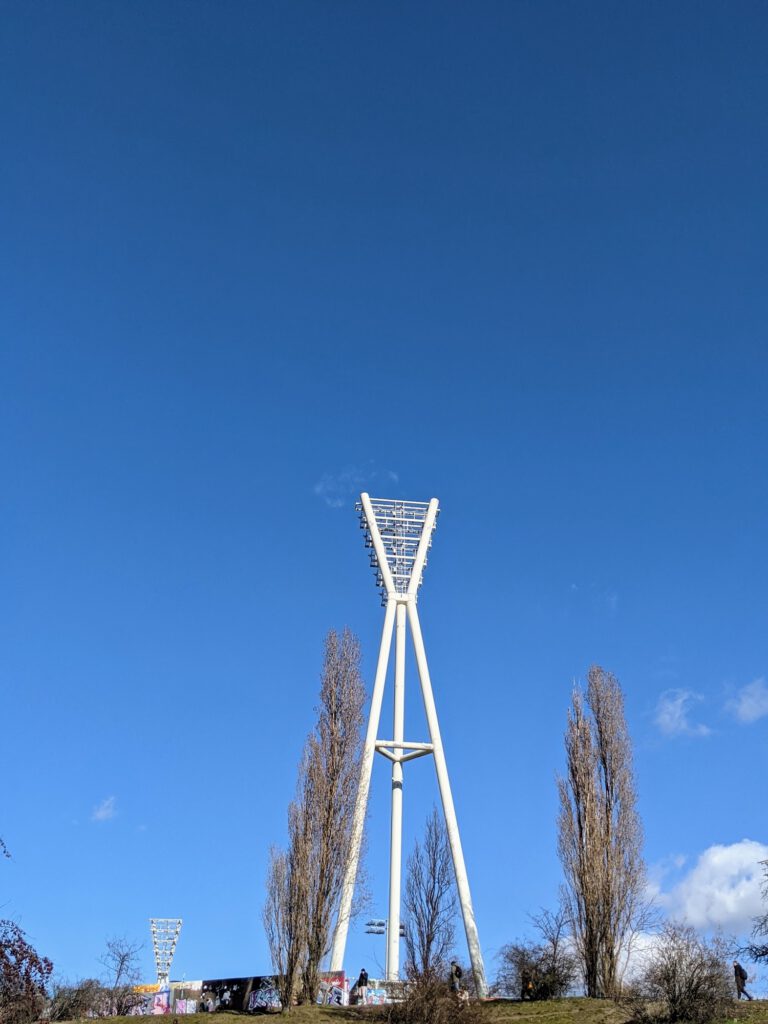 Weißer Flutlichtmast ragt zwischen kahlen Pappeln in den tiefblauen Himmel
