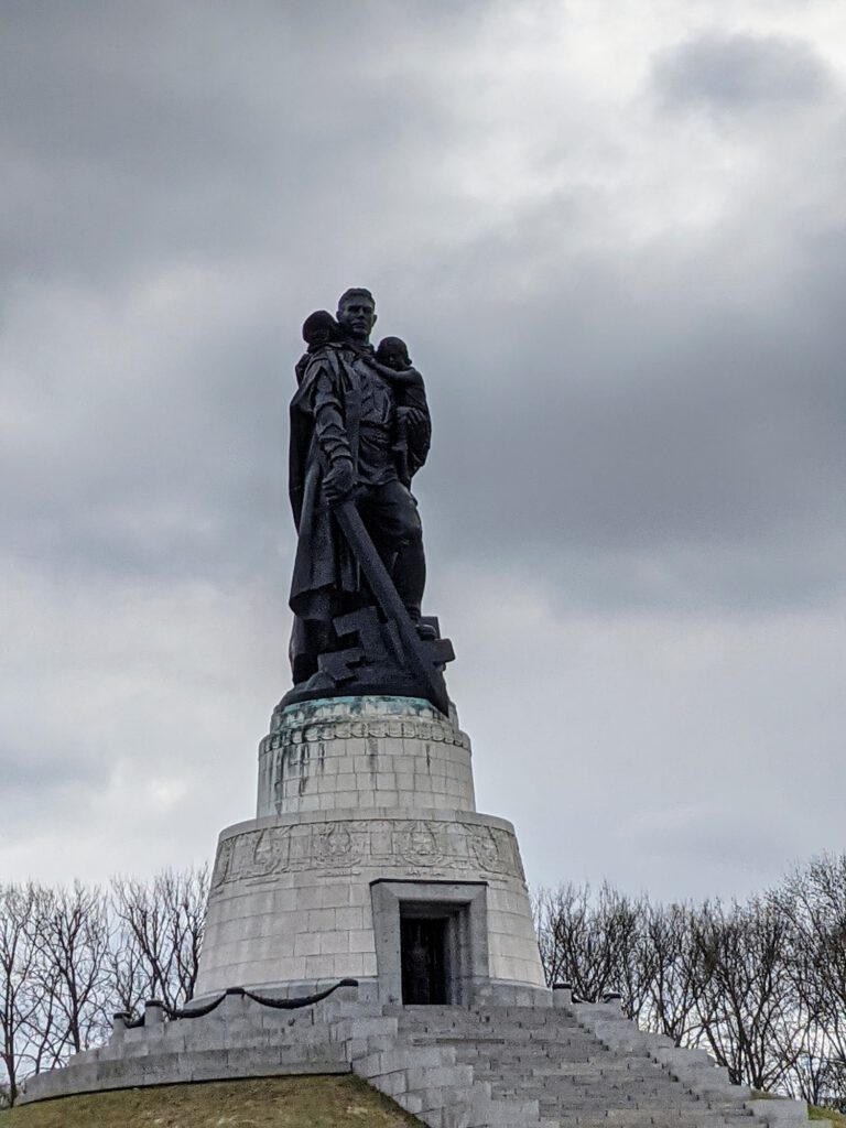 Bronzestatue eines Soldaten mit einem Kind auf dem Arm auf einem hohen Sockel über einem Grabhügel