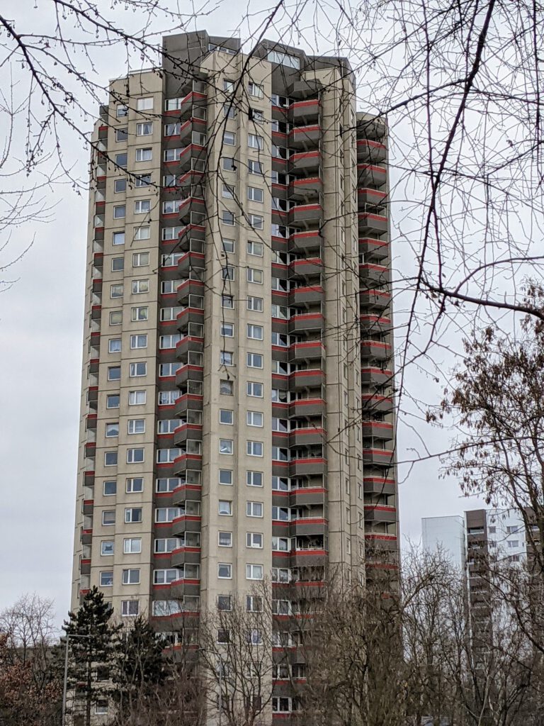 Wohnhochhaus mit roten Balkonen ragt hinter kahlen Bäumen auf