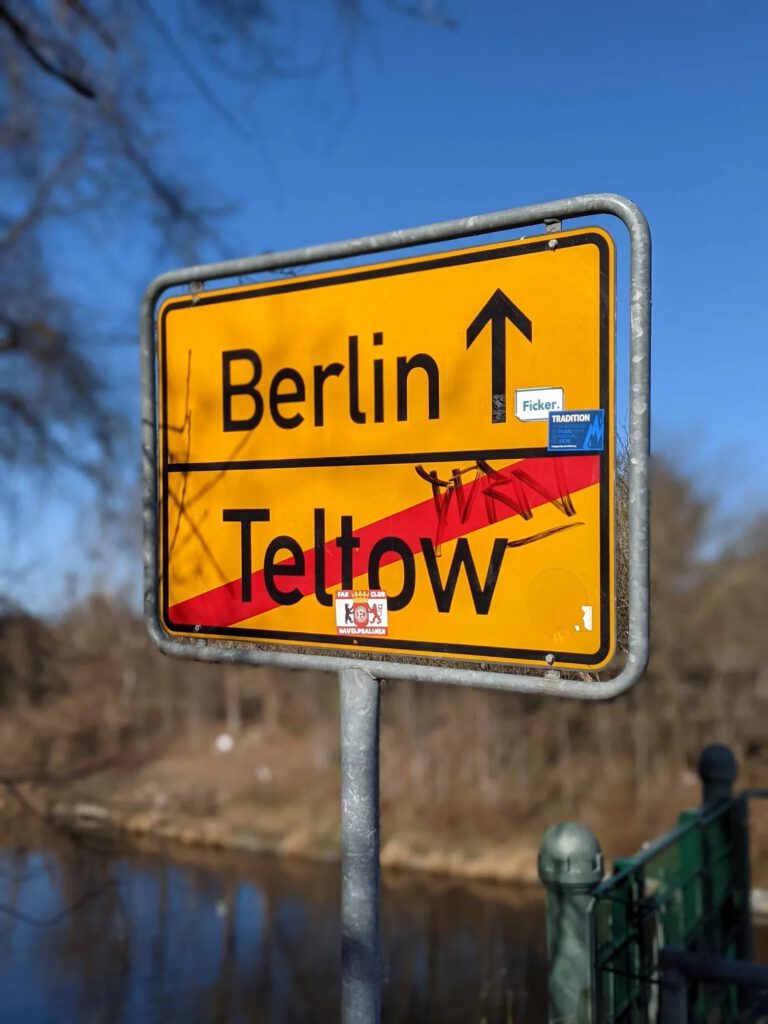 Zwei bemalte Mauersegmente auf einer Wiese: Auf einem fährt ein gelber Bus der Linie X10 über eine Brücke, darüber steht „Erst Trennung, dann Verbindung“