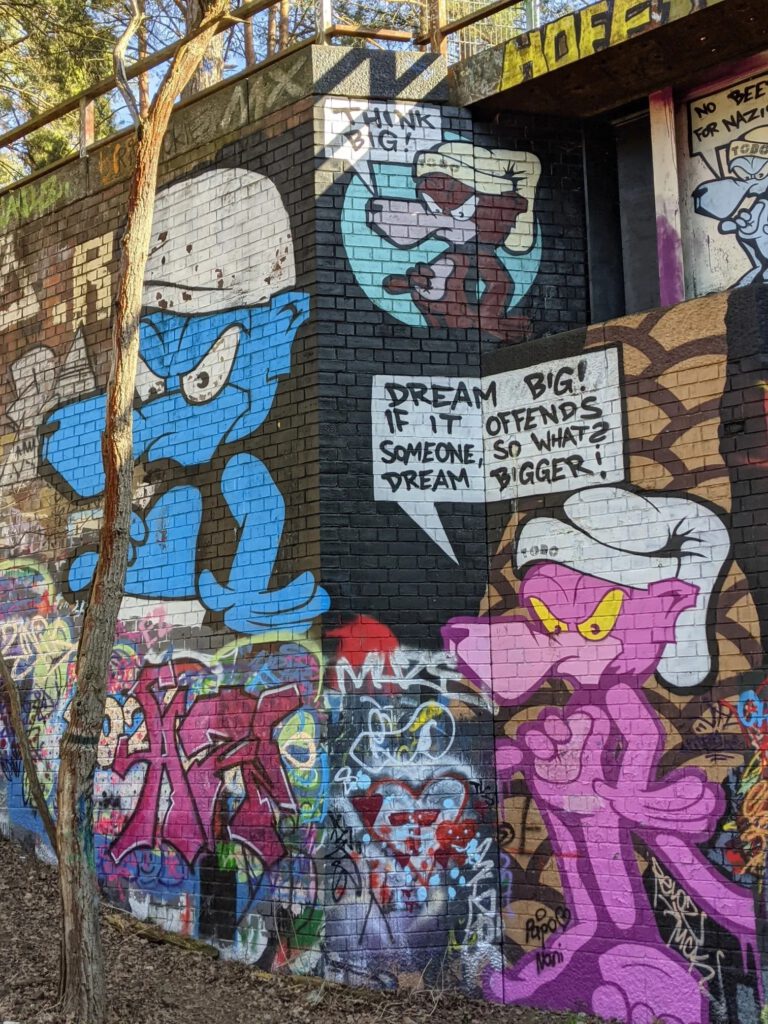 Bunt besprühtes Brückenwiderlager aus Backstein mit großen Comicfiguren in Blau und Pink und Sprechblasen
