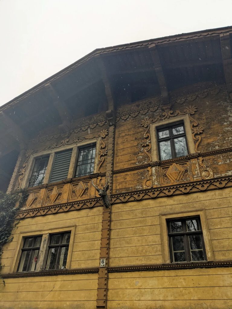 Ockerfarbene Hausfassade mit geschnitzten Verzierungen, weit überstehendem Dach und einem Hirschkopf an der Wand
