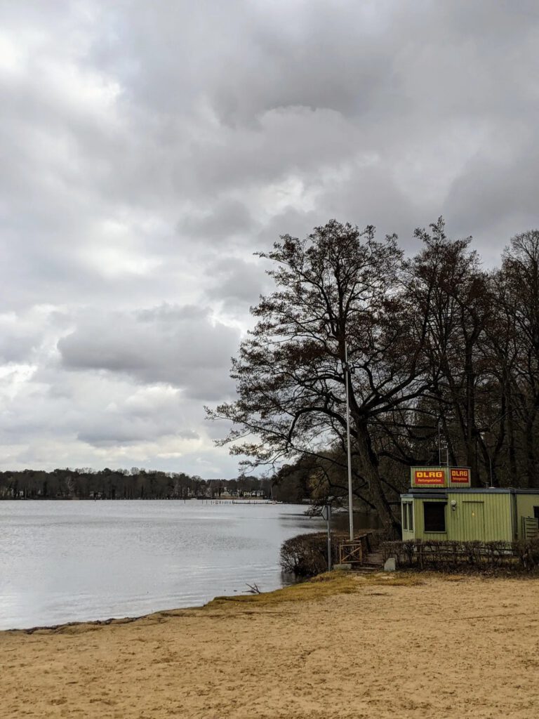 Sandstrand an der Havel mit einer grünen DLRG-Rettungsstation unter kahlen Bäumen