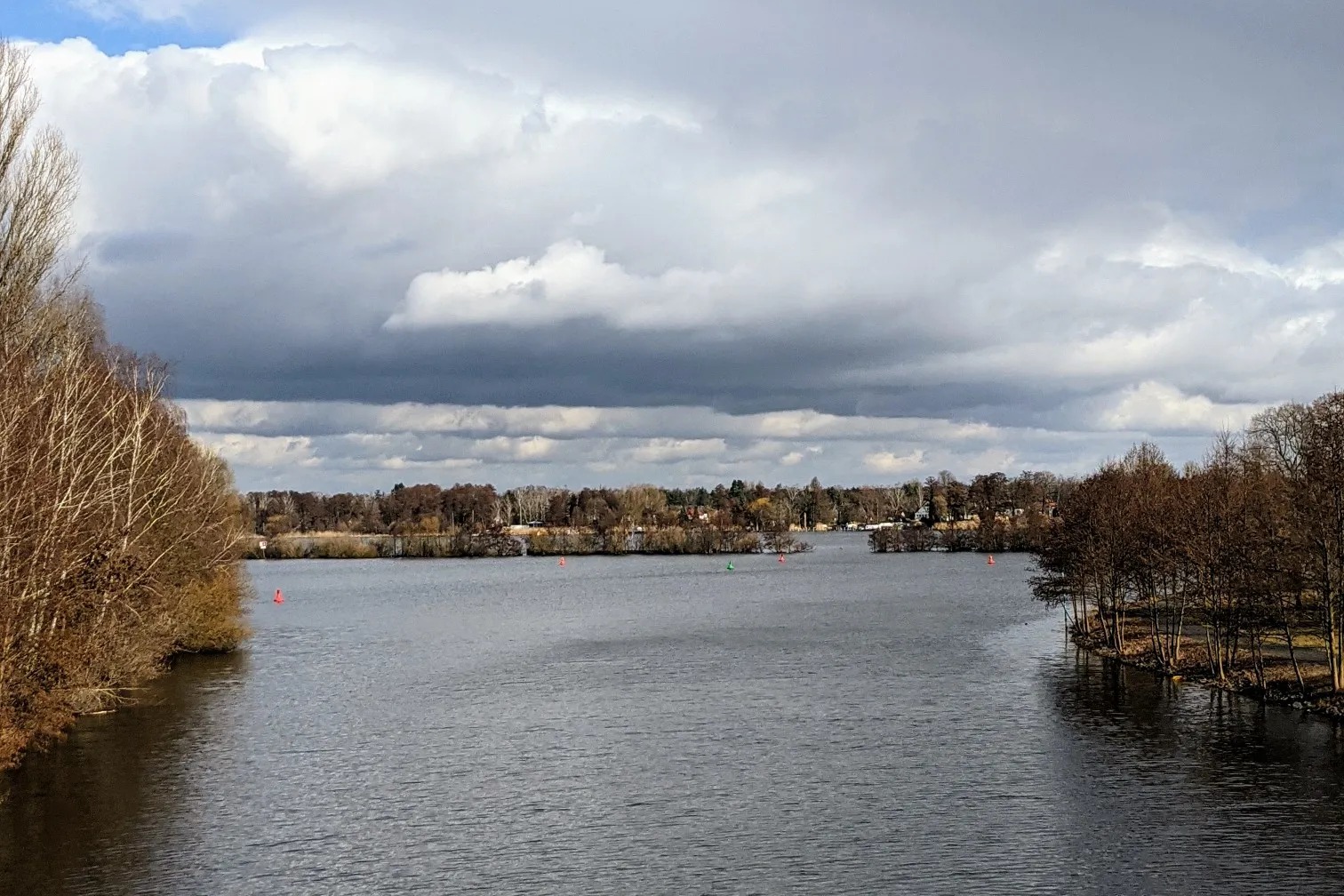 Blick von einer Brücke über eine breite Wasserfläche mit roten und grünen Tonnen, darüber hohe Wolken