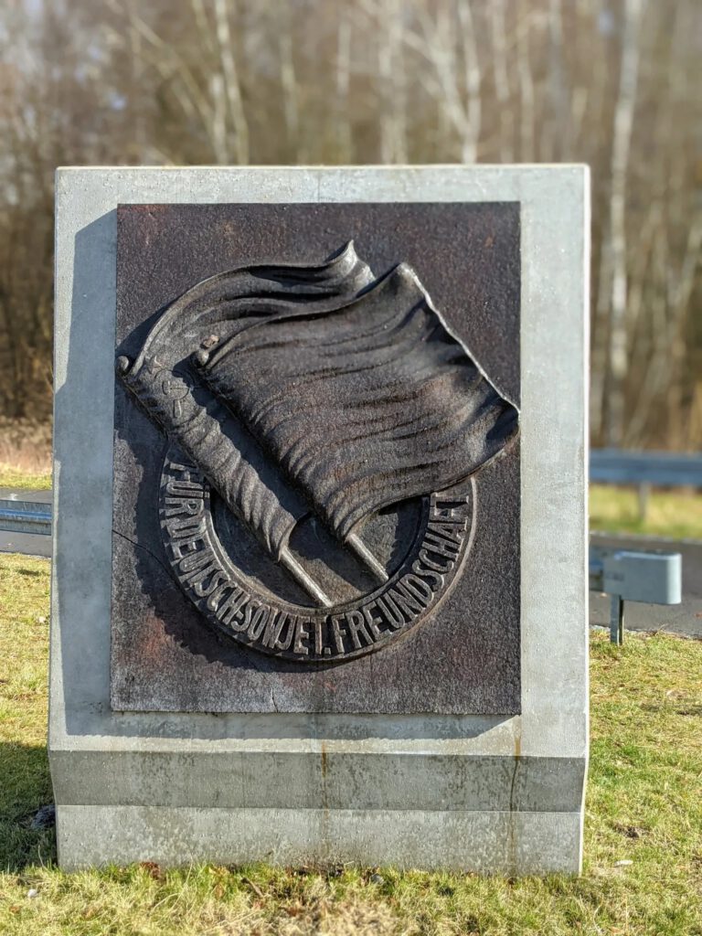 Betonstele mit einem Metallrelief zweier Fahnen und der Umschrift „Für deutsch-sowjet. Freundschaft“
