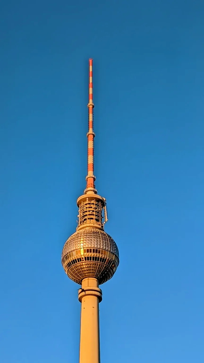 Fernsehturm am Alexanderplatz mit Kugel und rot-weißer Antenne im Abendlicht vor blauem Himmel
