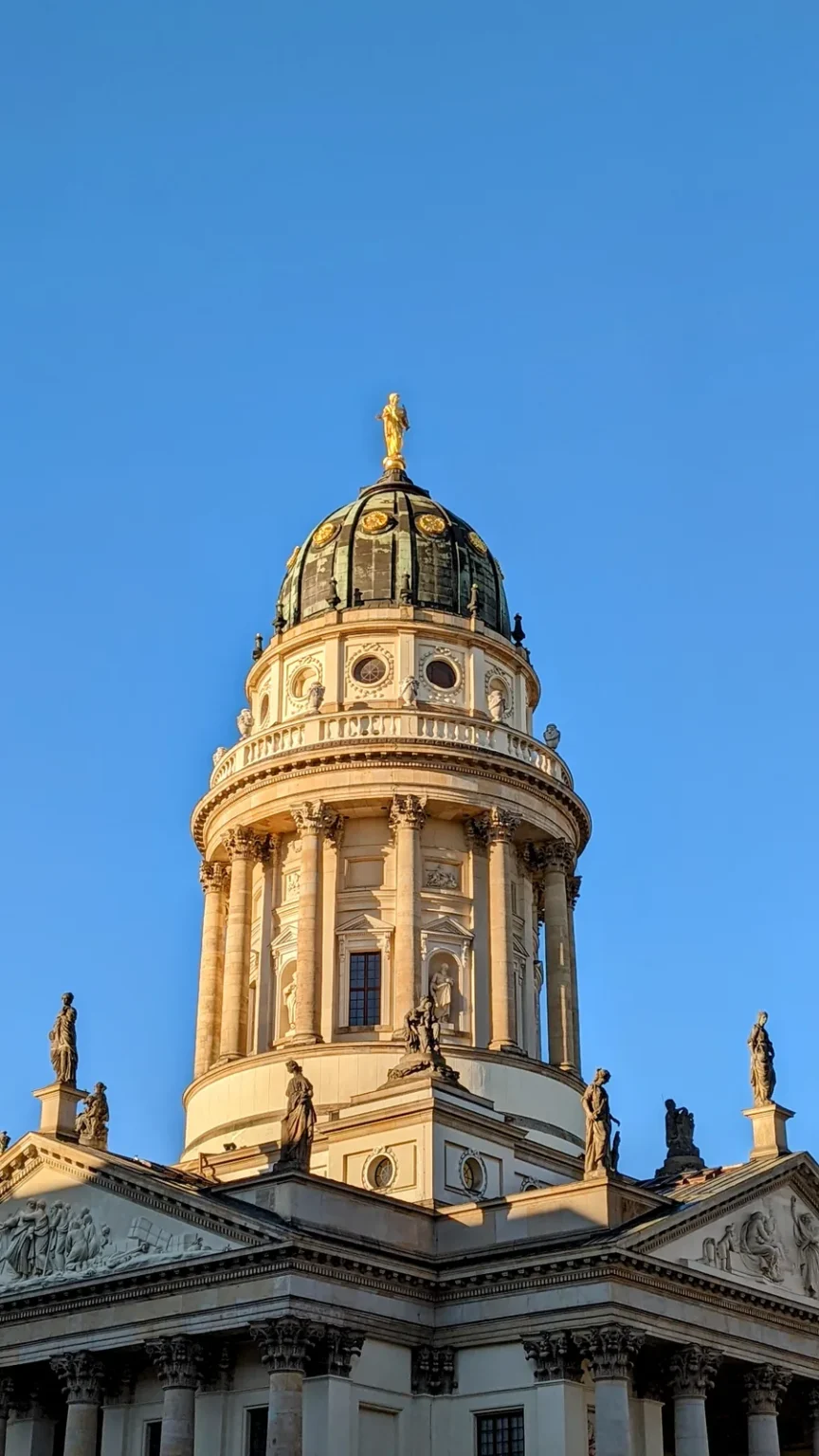 Kuppelturm des Französischen Doms am Gendarmenmarkt mit Säulen und Figuren vor blauem Himmel