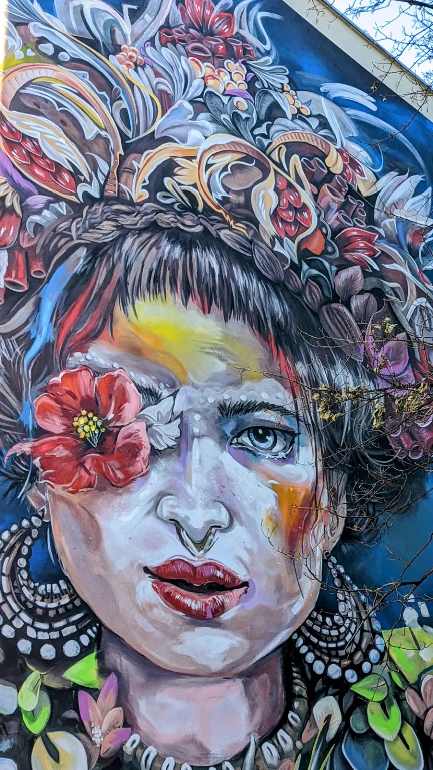 Wandbild von Wanda Stang: Frauengesicht mit großem Blumenkranz, eine rote Blüte vor einem Auge, Tucholskystraße 44