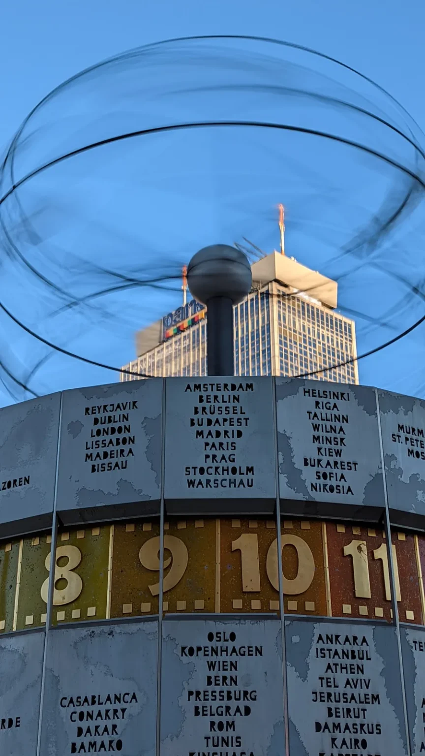 Weltzeituhr am Alexanderplatz mit Stundenzahlen, Städtenamen und dem Planetenmodell darüber, blauer Himmel
