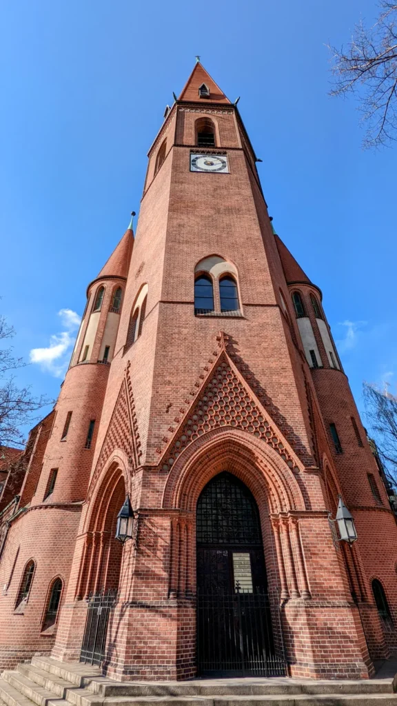 Backsteinturm der Heilige-Geist-Kirche in Moabit mit Uhr, Spitzbogenportal und zwei runden Treppentürmen