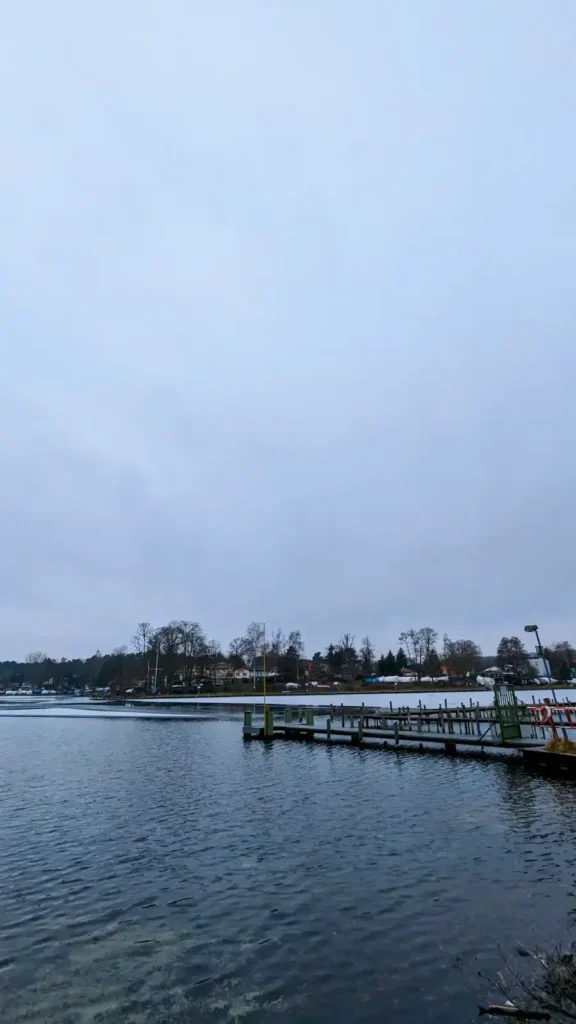 Steg am Westufer der Großen Krampe in Müggelheim im Winter, dahinter das Wasser und kahler Wald