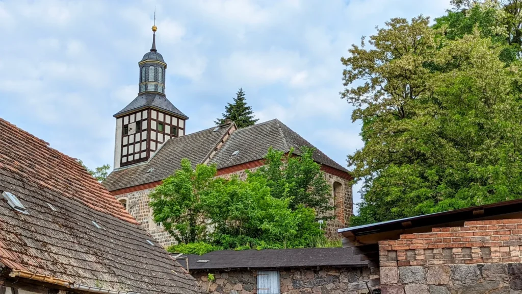 Dorfkirche Niederfinow mit Fachwerkturm und Laterne hinter Ziegeldächern und einer Backsteinmauer