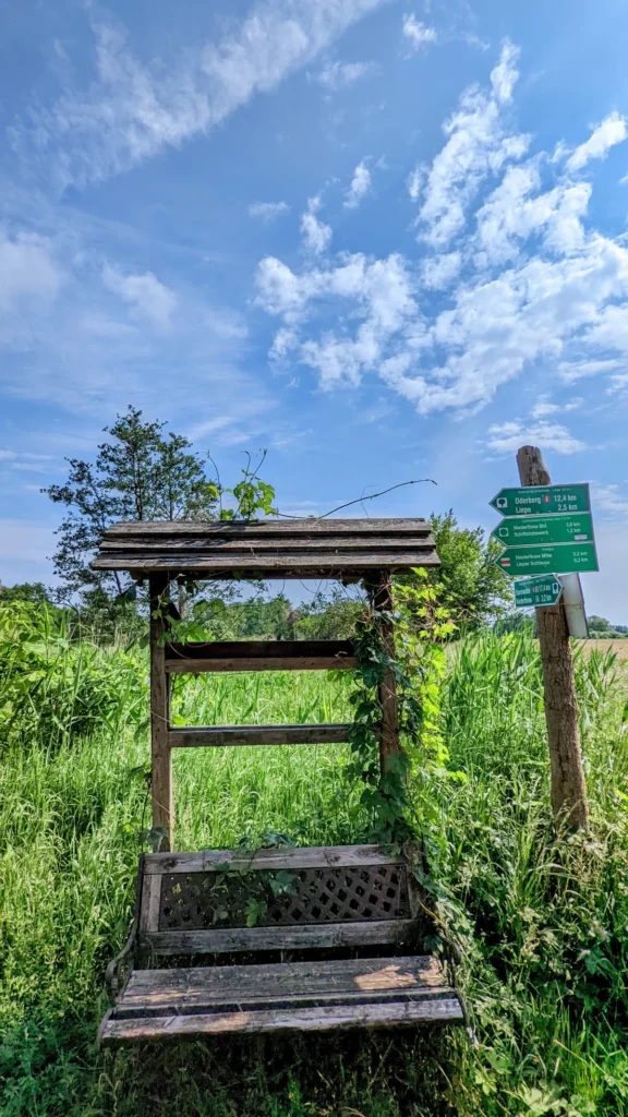 Überdachte Holzbank mit grünem Wegweiser nach Oderberg und Liepe am Rand einer Wiese
