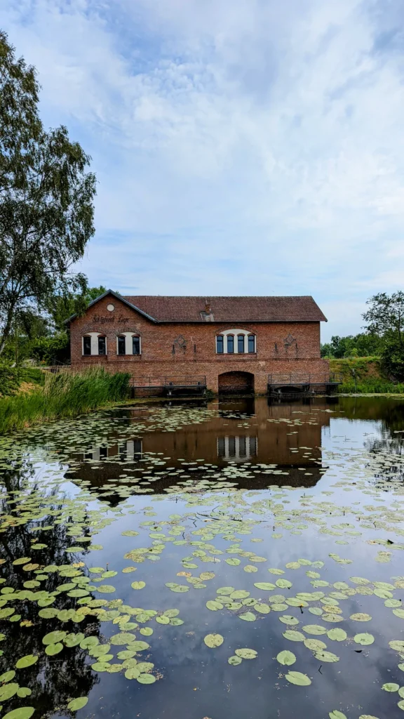 Schöpfwerk Liepe, ein Backsteinbau mit Rundbogendurchlass direkt an der Alten Finow, im Wasser Seerosenblätter