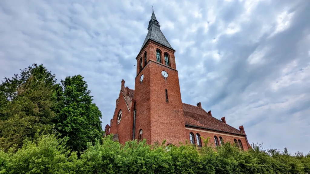 Dorfkirche Neuenhagen aus rotem Backstein mit Turmuhr hinter einer Hecke