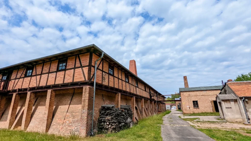 Langes Trockengebäude aus Backstein und Fachwerk an der Ziegelei Altglietzen, dahinter ein Schornstein