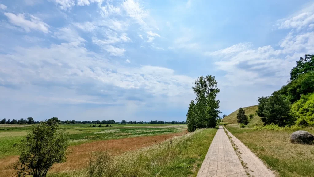 Gepflasterter Weg am Fuß eines Hangs bei Altglietzen, links weite Felder des Oderbruchs