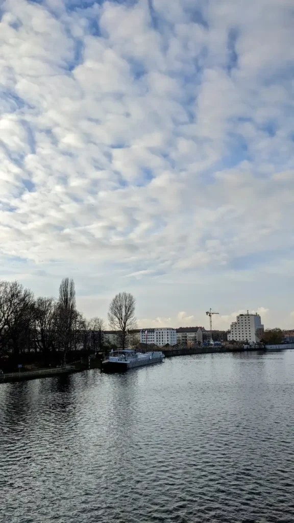 Die Spree zwischen Niederschöneweide und Oberschöneweide mit Schiffen am Ufer unter einem wolkigen Himmel